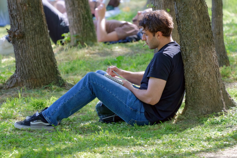 Boy smoking, leaning by a tree trunk